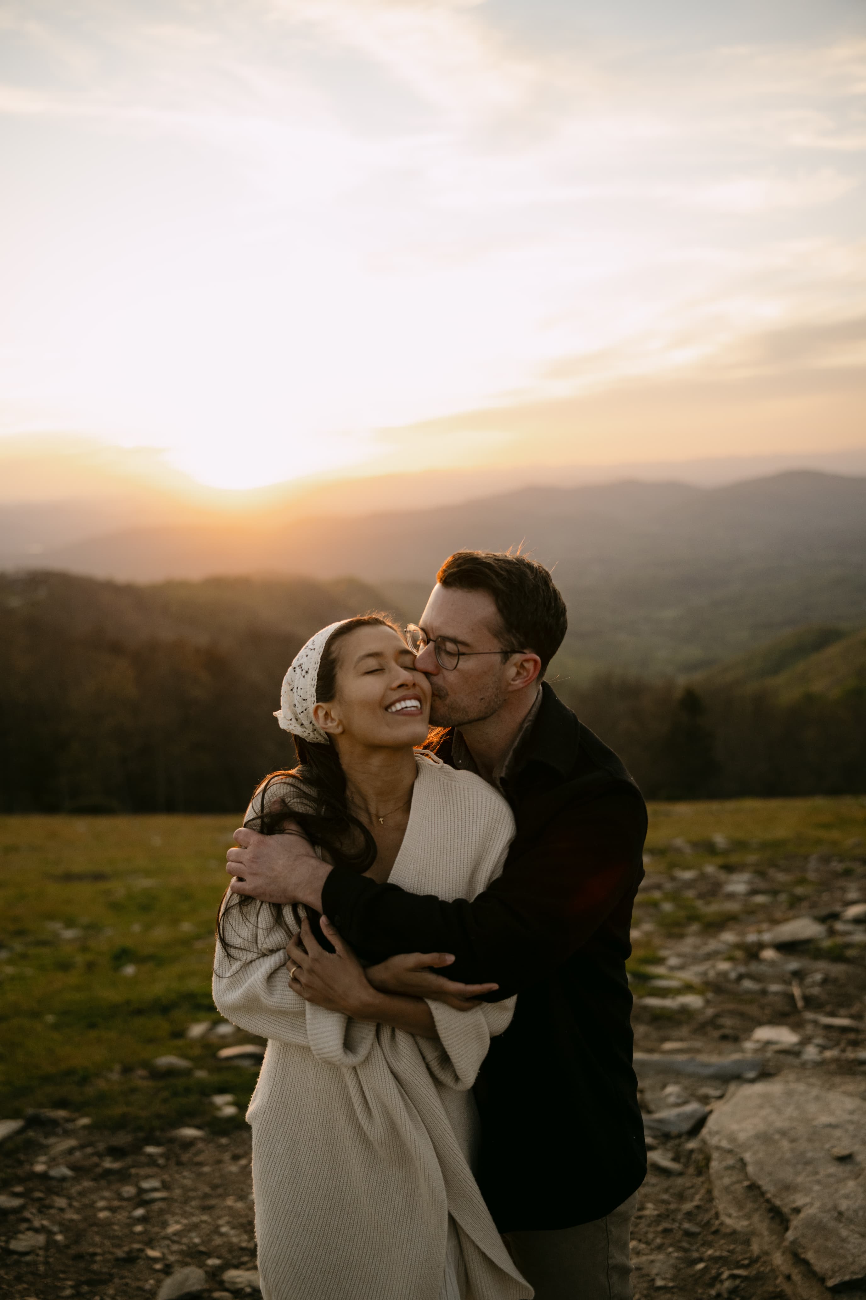 Daniel kissing Michal's cheek at golden hour, the Blue Ridge Mountains behind them