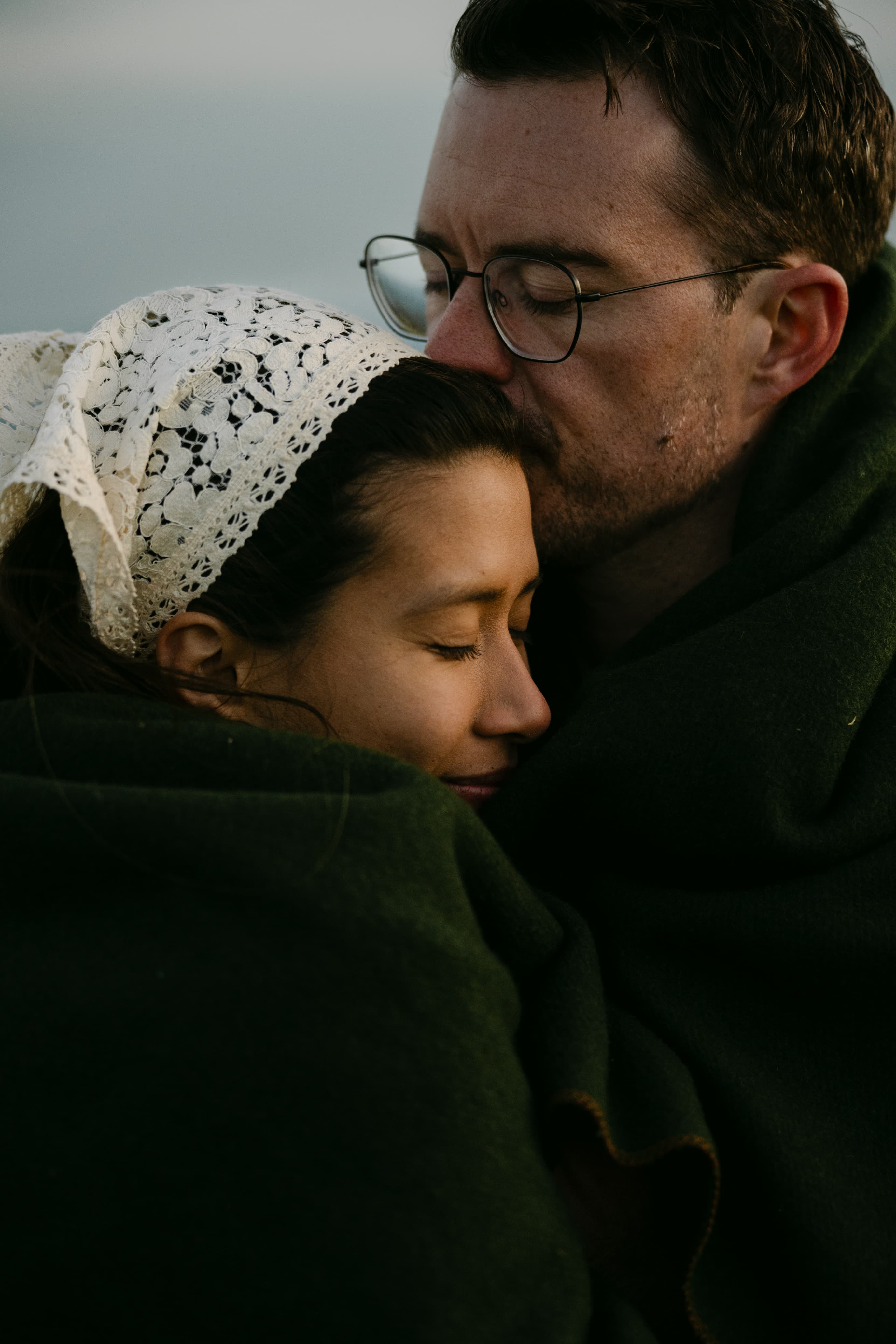 Daniel and Michal wrapped in a green wool blanket, his lips resting on her forehead