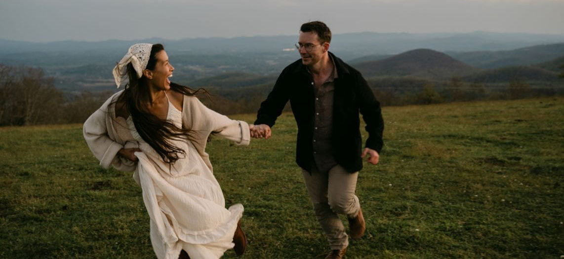 Daniel and Michal running hand in hand across a mountain meadow, laughing